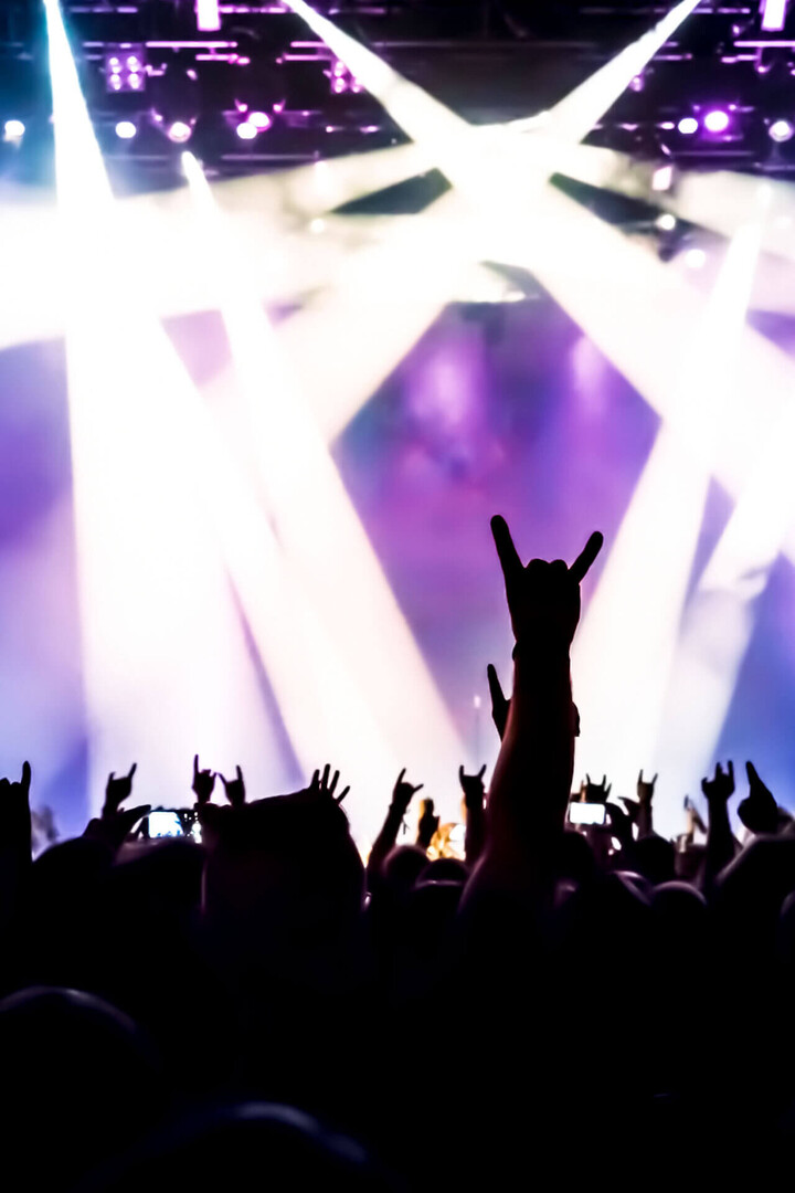 Konzertpublikum mit erhobenen Händen und bunten Lichtstrahlen auf der Bühne